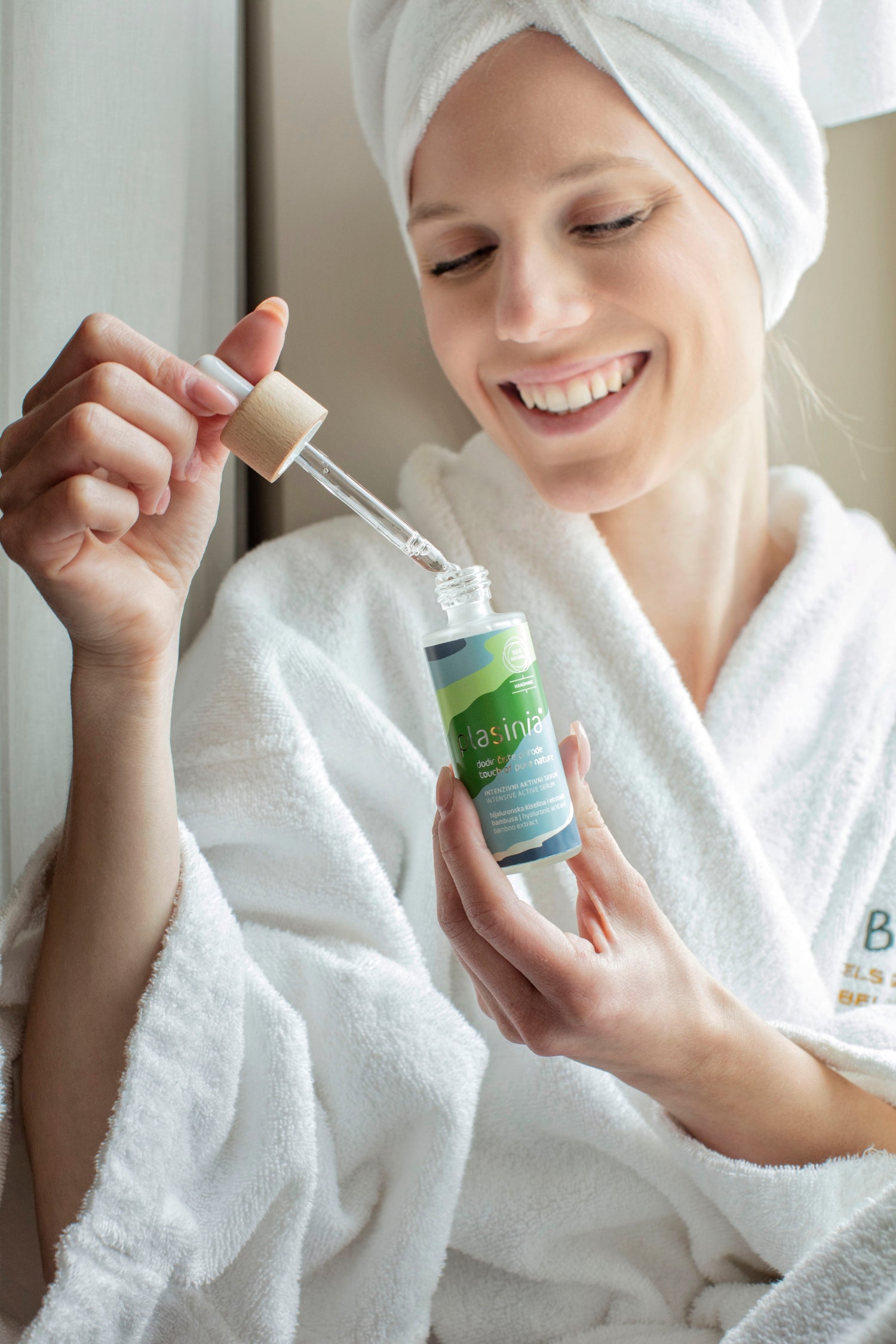 Woman in a white robe holding a bottle of skincare product with a dropper.